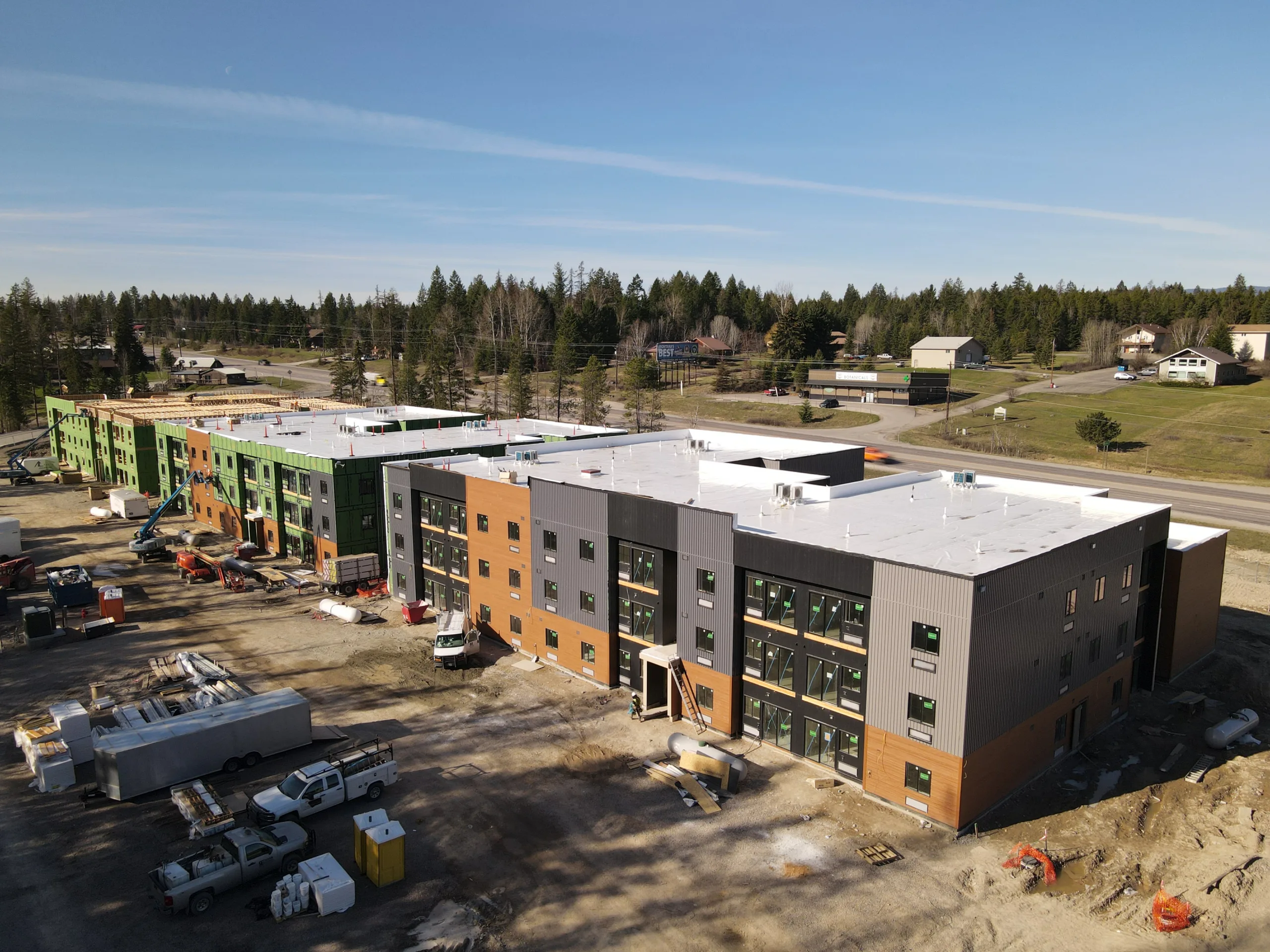 Drone view of Alpine 93/40 showing multiple residential buildings under construction, with active site work, construction equipment, and surrounding forested landscape.